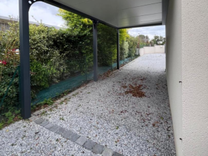 Carport anthracite long adossé, toit blanc sur allée gravier et haie verte