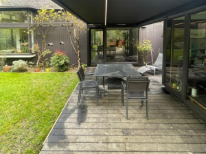 Store banne noir avec bandeau LED sur terrasse bois, table et transat gris