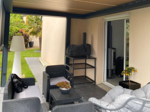 Terrasse pergola anthracite, salon rotin gris et poêle visible par baie vitrée
