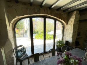 Baie cintrée anthracite vue salle à manger, poutres bois et lilas sur table