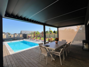 Pergola bioclimatique noire lames fermées, table grise sur deck, piscine turquoise