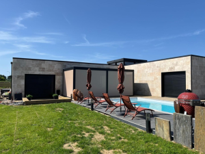 Façade pierre claire, pergola noire stores beige, piscine et transats terracotta