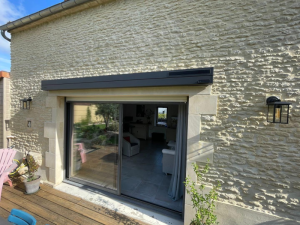 Volet roulant solaire anthracite au-dessus baie, mur pierre et appliques noires