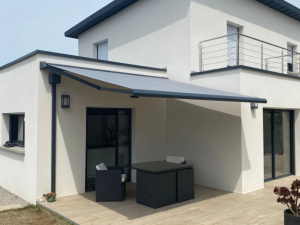 Store banne gris clair déployé sur terrasse d'une maison blanche à menuiseries sombres