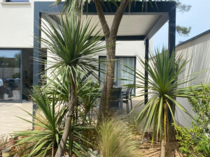 Pergola bioclimatique blanche et anthracite sur terrasse entourée de végétation exotique