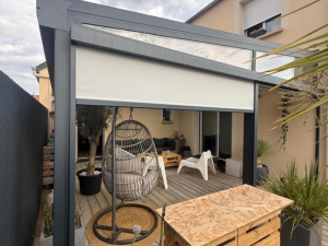Pergola grise vitrée, store latéral beige, fauteuil oeuf rotin et comptoir palettes