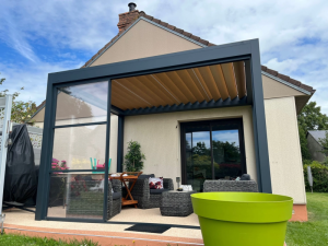 Pergola bioclimatique anthracite, lames bois et paroi vitrée coulissante sur terrasse