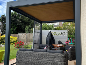 Sous pergola anthracite, plafond lames bois, salon résine gris et haie verte