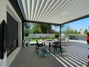 Pergola lames blanches, stores latéraux zip et table blanche sur carrelage