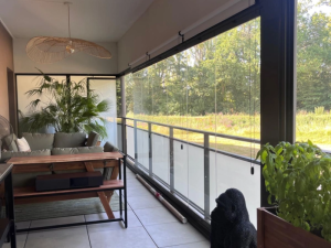 Balcon fermé rideau de verre, canapé vert, suspension rotin et jardin lumineux