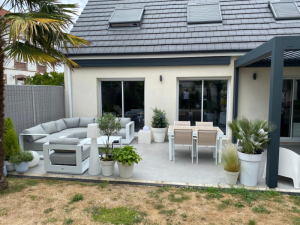 Terrasse carrelée, store banne anthracite, salon blanc et pergola au fond