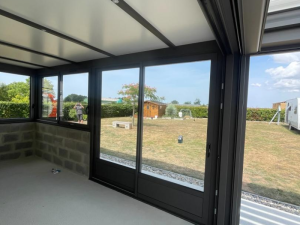 Intérieur véranda en chantier, baies anthracite sur parpaings et jardin ensoleillé