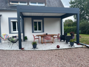 Pergola bioclimatique grise lames claires, table ovale et chaises saumon sur dalles