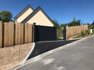 Portail coulissant anthracite entre clôture planches bois, allée enrobée noire et maison crème