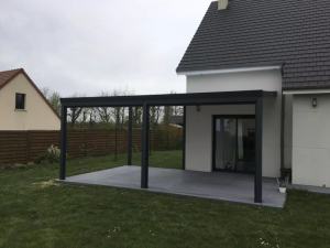 Pergola adossée anthracite toit plat sur terrasse composite grise, pelouse et clôture bois