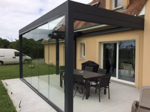 Pergola anthracite parois vitrées coulissantes, table grise et barbecue sur dalle béton