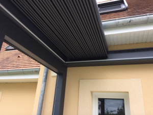 Détail lames orientables anthracite sous pergola adossée à façade beige et gouttière zinc