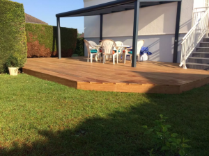 Pergola noire sur terrasse bois neuf, table ronde blanche et haie verte