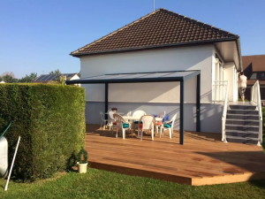 Pergola anthracite toit translucide, salon blanc sur terrasse bois devant pavillon