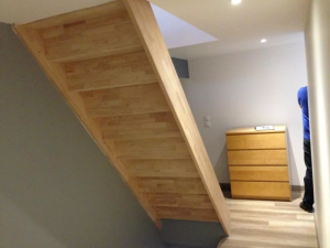 Escalier bois clair marches pleines, mur gris, spots encastrés et commode assortie