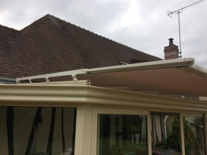 Gros plan store toiture creme sur veranda, toit tuiles marron et ciel nuageux