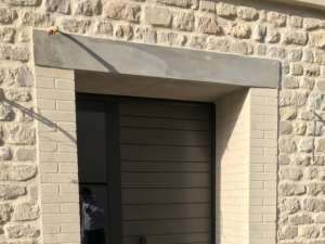 Porte garage anthracite lames horizontales dans mur pierre, linteau béton gris
