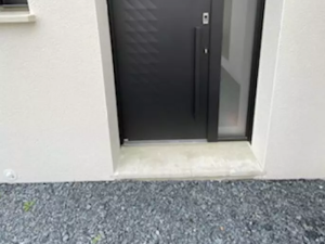 Porte anthracite et tierce vitree depolie sur facade creme, gravier devant le seuil