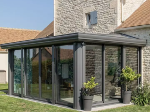 Veranda anthracite sur maison pierre, fauteuil suspendu visible derriere vitrage