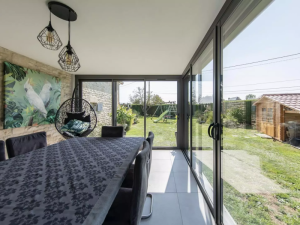Interieur veranda, baies noires sur jardin, table a manger et suspensions filaires