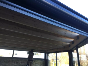 Chantier veranda, charpente bois sous toit noir, mur pierre et baies posees