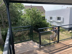 Garde-corps vitre noir sur terrasse sur pilotis, jardin et maison blanche