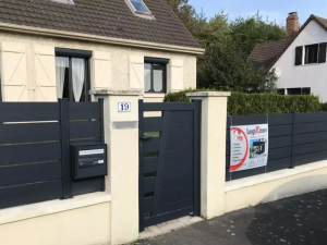 Portillon et cloture grises sur muret beige devant maison a volets creme