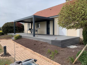 Pergola bioclimatique anthracite sur terrasse composite grise, table verte