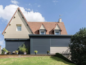 Facade bardage beige, quatre volets roulants gris fermes sous toit tuiles