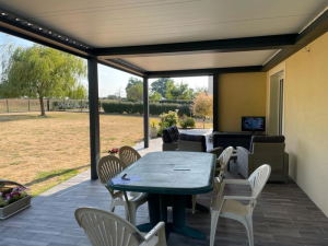 Pergola bioclimatique noire toit blanc, table verte et fauteuils gris sur dalle