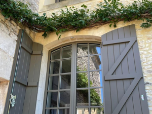 Fenêtre cintrée taupe petits bois, volets ouverts croisillon Z sur mur pierre