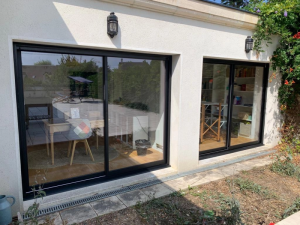 Deux baies coulissantes noires sur facade crepi, applique et reflet terrasse