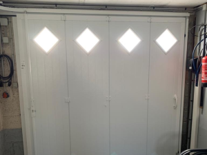 Porte garage pliante blanche quatre vantaux, hublots losange vue intérieur garage