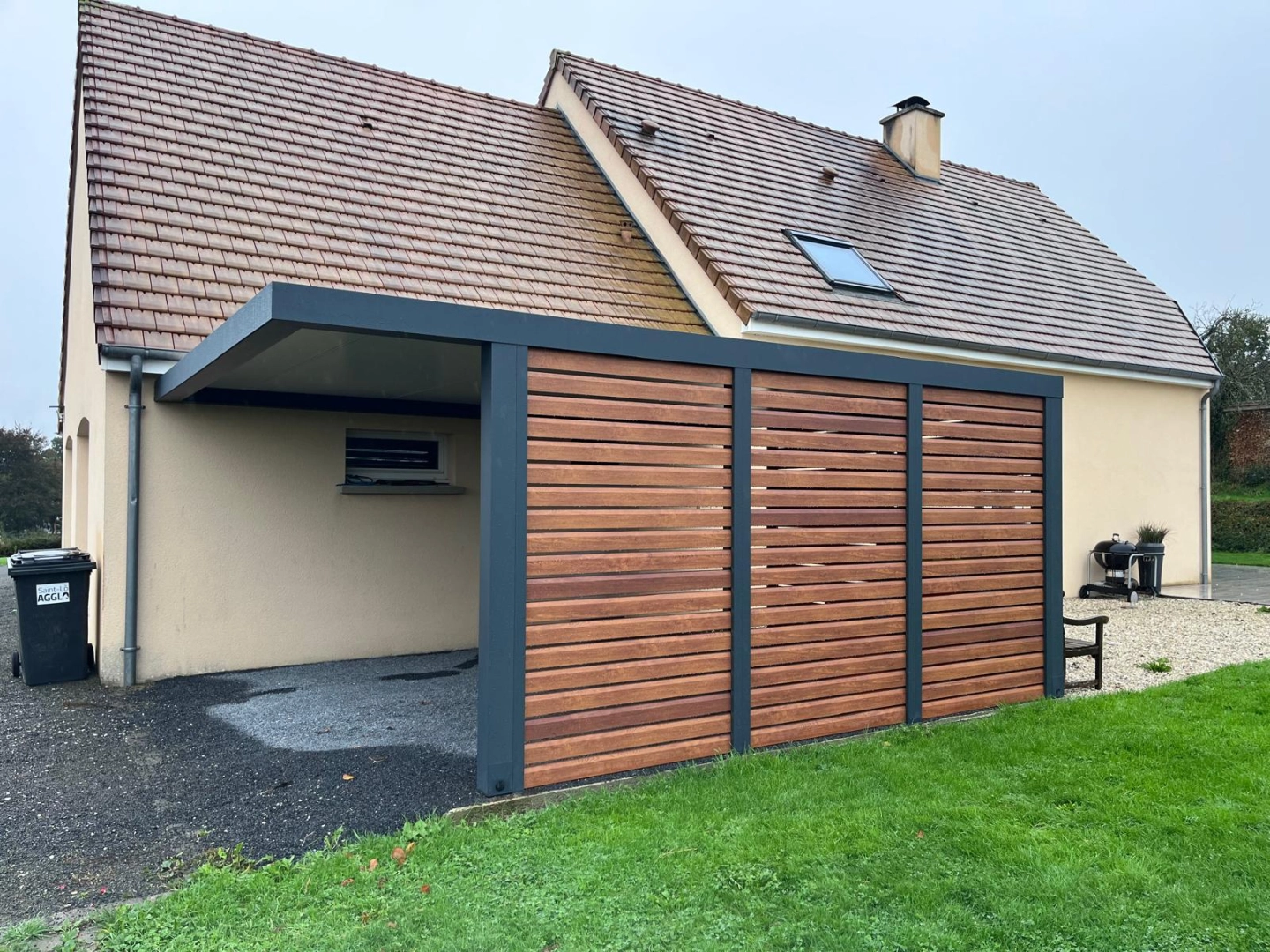 Carport anthracite toit plat, claustra bois horizontal, adossé à maison tuiles brunes