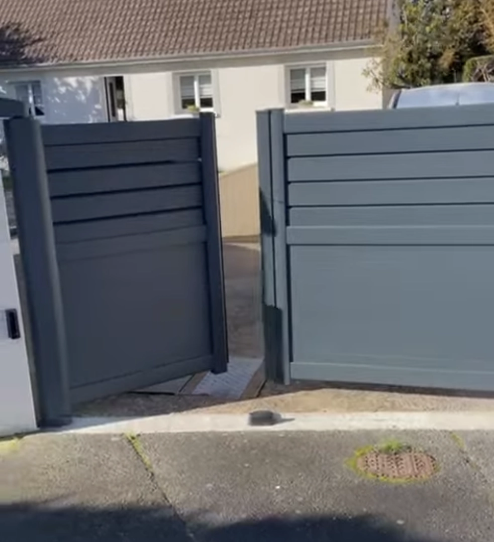 Portail battant alu anthracite mi-clair à lames, un vantail ouvert sur allée béton