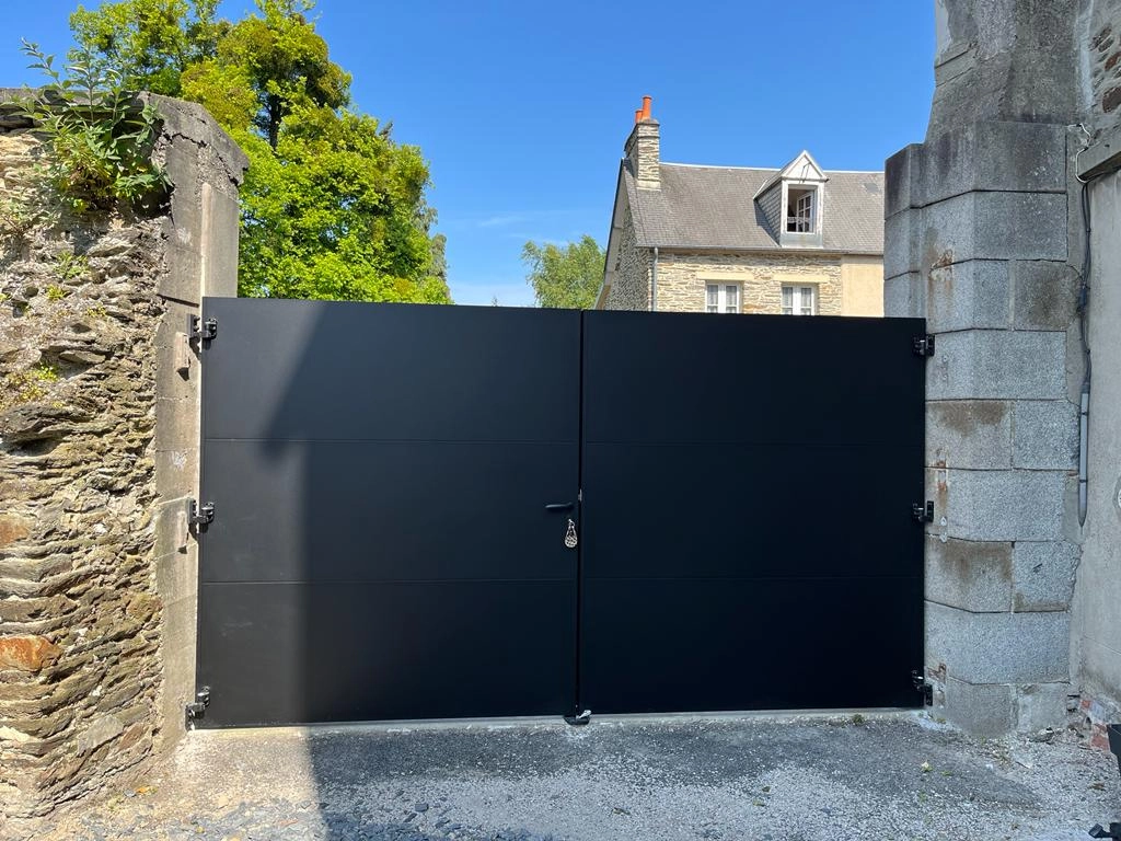 Portail battant noir mat lames pleines, mur pierres sèches et pilier granit