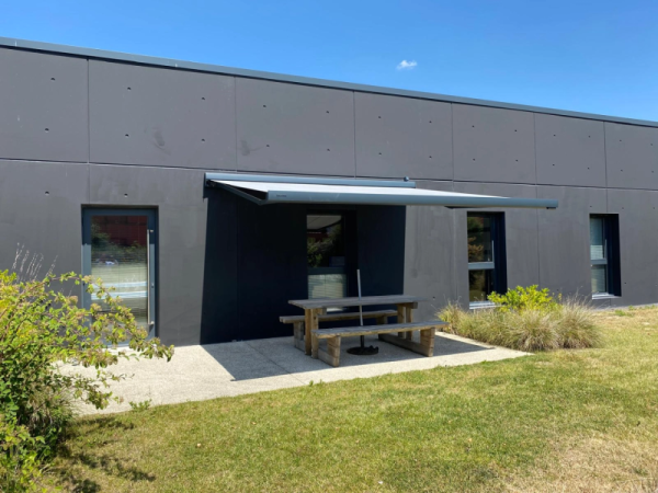 Store banne gris clair marque HAROL sur façade anthracite, table pique-nique bois
