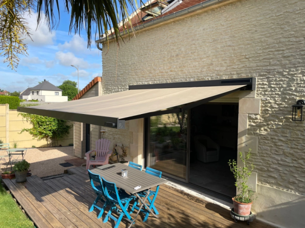 Store banne beige coffre anthracite, terrasse bois pierre et chaises turquoise