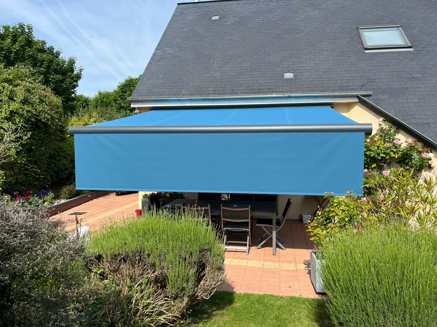 Store banne bleu déployé sur terrasse carrelée orange, rosiers grimpants