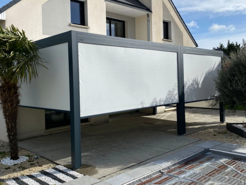 Pergola anthracite avec stores verticaux blancs sur terrasse béton, piscine au premier plan