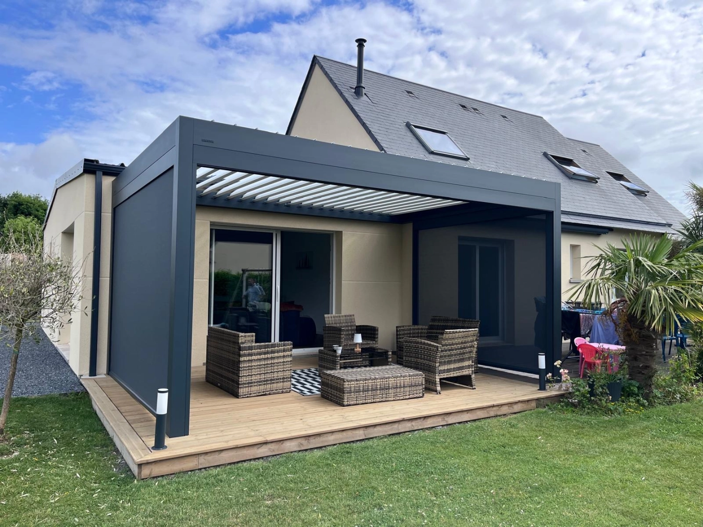 Pergola bioclimatique anthracite, lames blanches, store mesh et salon rotin