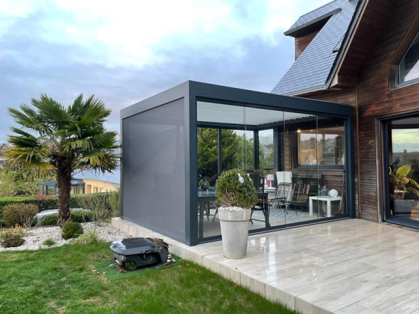 Pergola bioclimatique anthracite, store latéral, parois vitrées, terrasse bois et palmier