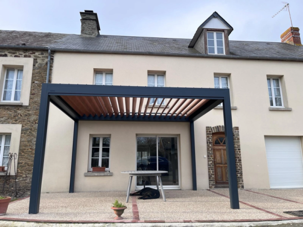 Pergola bioclimatique alu anthracite, lames ton bois, terrasse pavée devant maison en crépi