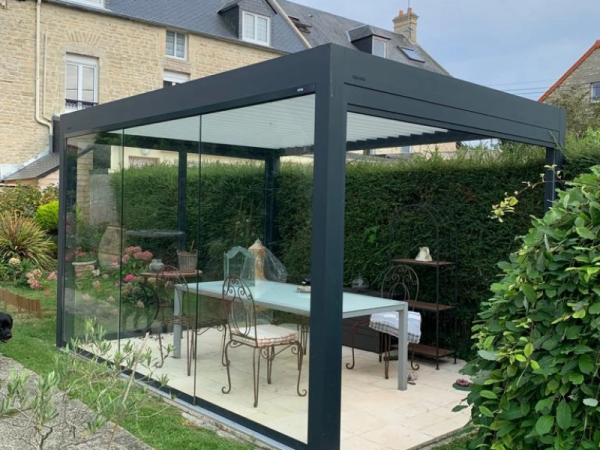 Pergola bioclimatique anthracite, lames blanches, parois vitrées coulissantes, dalles beige