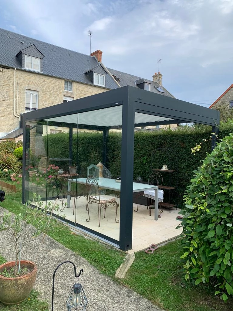 Pergola bioclimatique anthracite, lames blanches, parois vitrées coulissantes, dalles beige